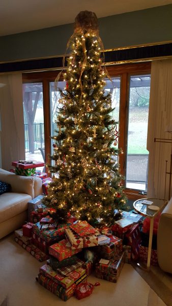 The gifts are packed tightly under the tree and extend behind the tree on both sides.